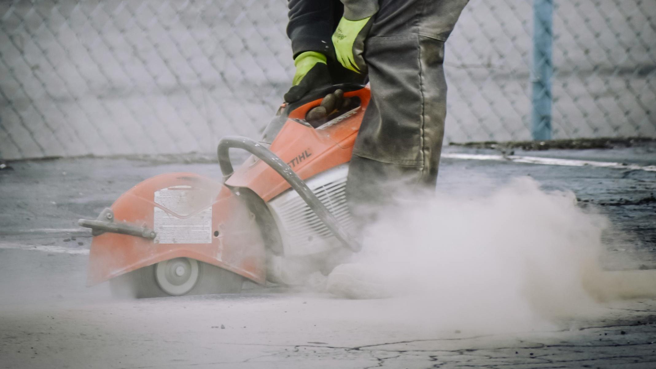 Worker with protective gear cutting concrete with a saw in an outdoor setting.